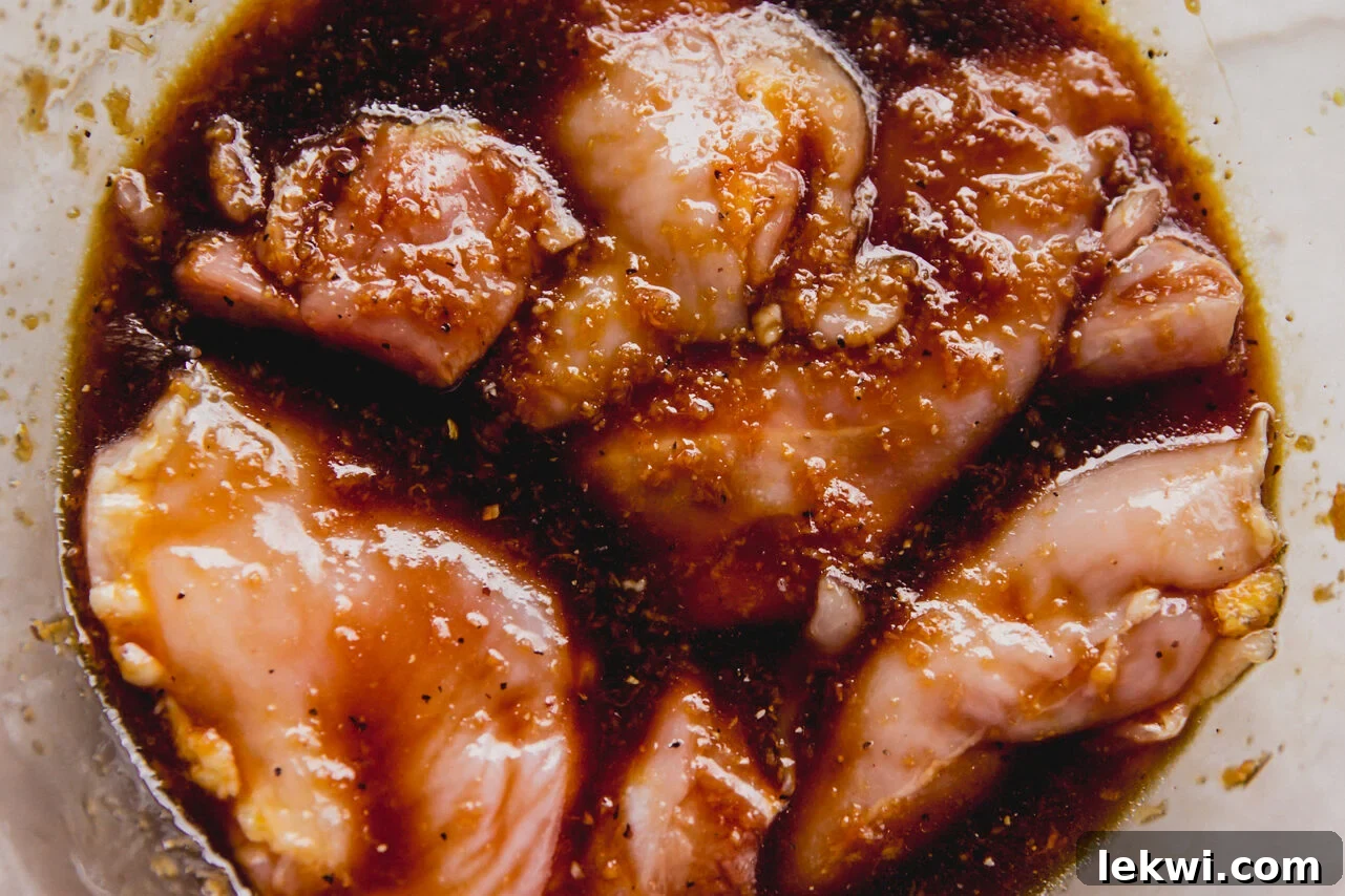 Chicken thighs marinating in a flavorful sauce in a clear glass bowl, ready to absorb all the delicious flavors.