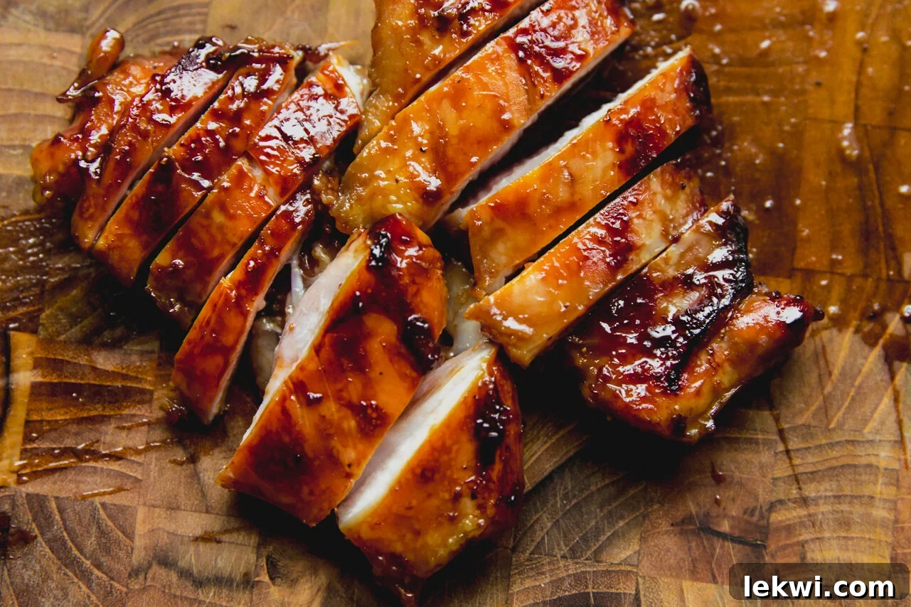 Two perfectly cooked and sliced chicken thighs resting on a rustic wooden cutting board, ready to be added to the broth.