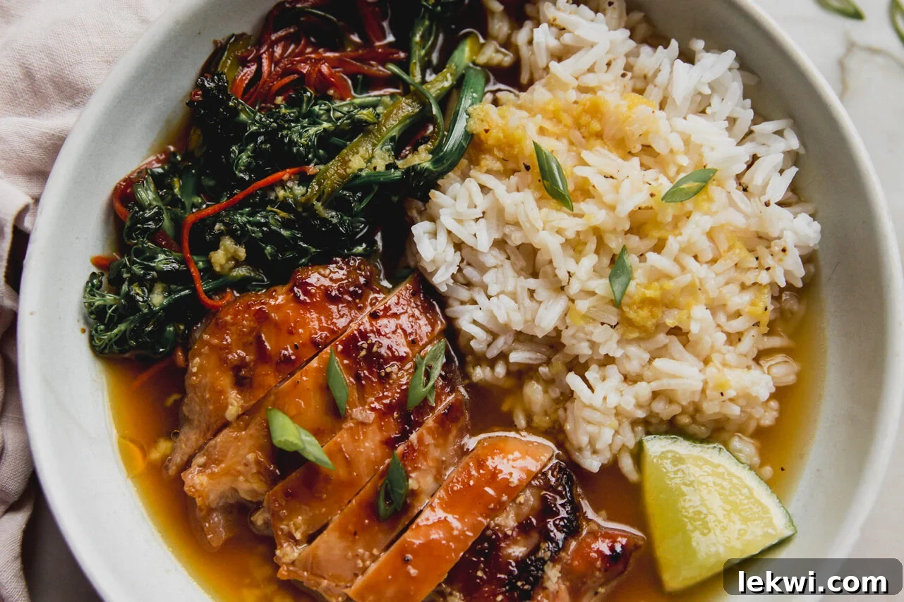 The fully assembled brothy ginger chicken and rice bowl, adorned with sliced chicken, sautéed vegetables, rice, green onions, and a lime wedge, ready to be enjoyed.