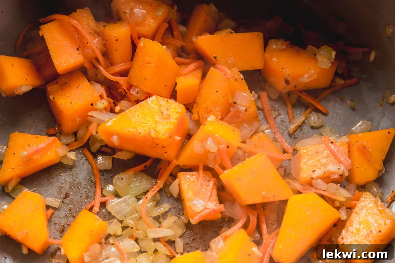 Butternut squash, shredded carrots and onions being sautéed in a large pot, creating a fragrant and flavorful base for the soup.