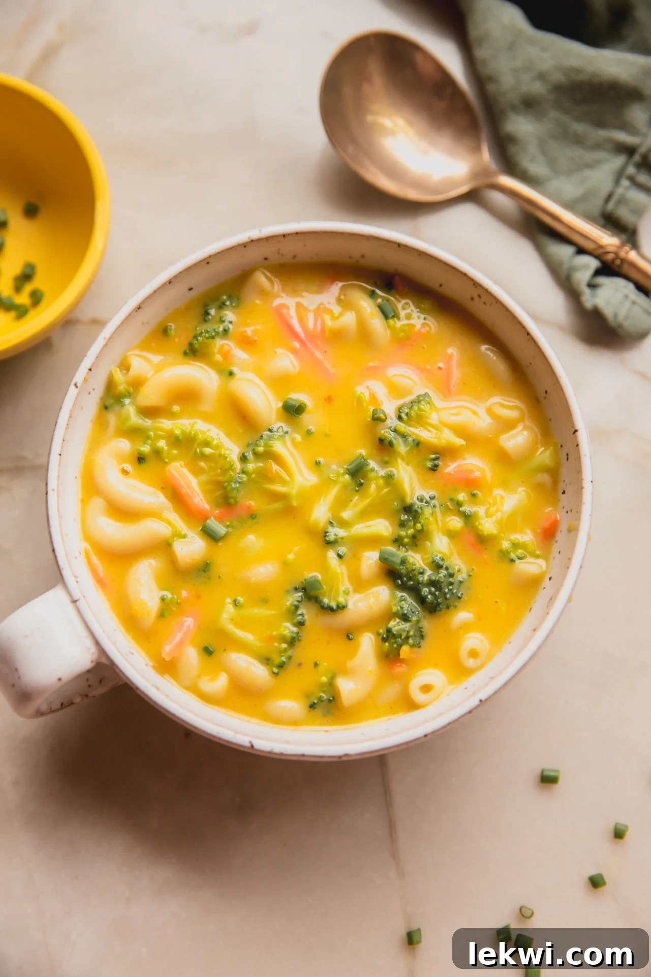 A beautiful bowl of dairy-free and gluten-free broccoli cheese noodle soup, garnished with fresh chives, ready to be enjoyed with a spoon.