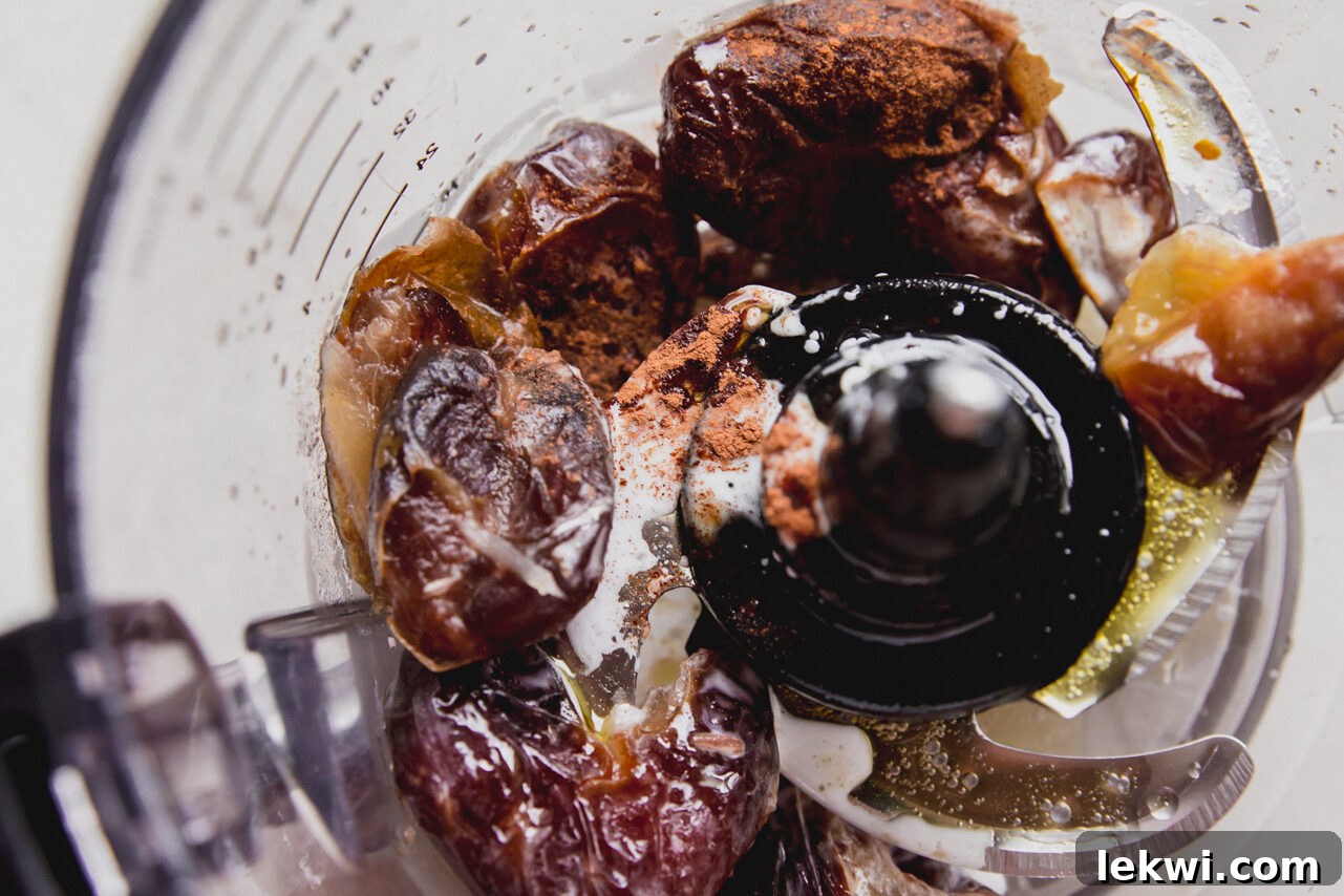 A food processor blending softened dates, ghee, and cinnamon into a thick, sticky date swirl filling.
