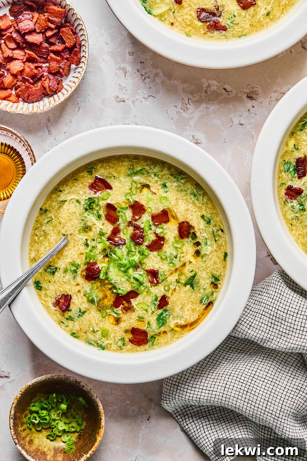 Breakfast egg drop soup in a bowl topped with bacon and green onion, with bacon on the side.