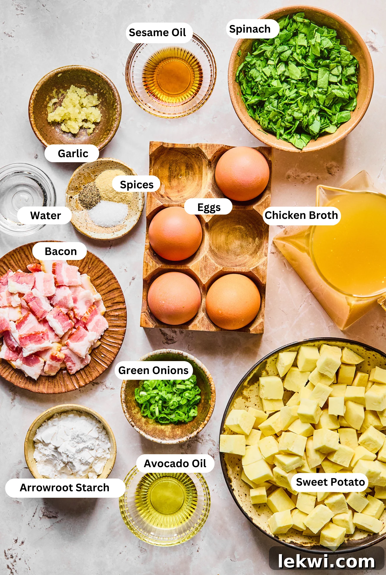 All fresh ingredients neatly arranged in separate bowls, ready for preparing the Breakfast Egg Drop Soup: eggs, water, chopped bacon, diced Japanese sweet potato, minced garlic, avocado oil, chicken bone broth, salt, pepper, onion powder, arrowroot starch, spinach, sesame oil, and chopped green onion.