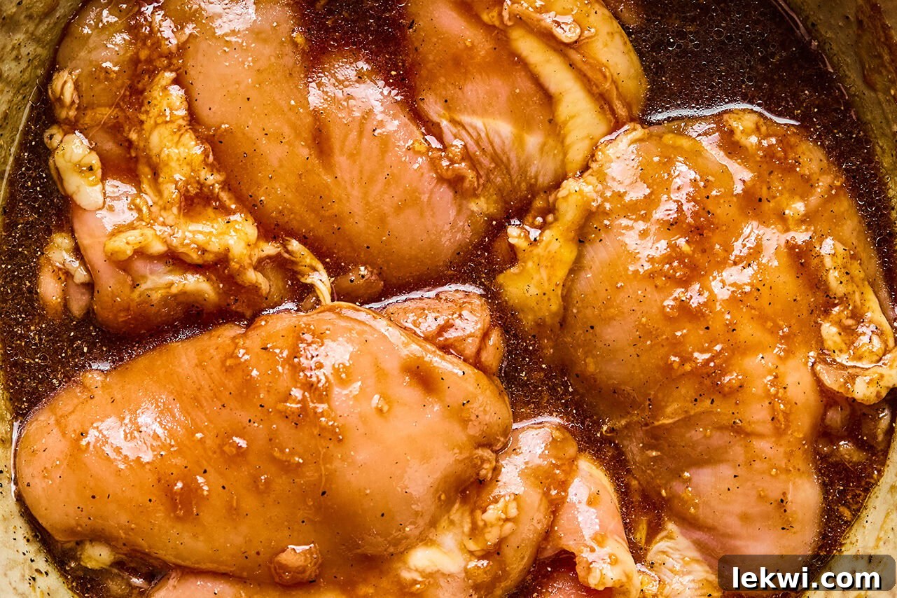 Chicken thighs marinating in a bowl, coated in a rich teriyaki sauce.