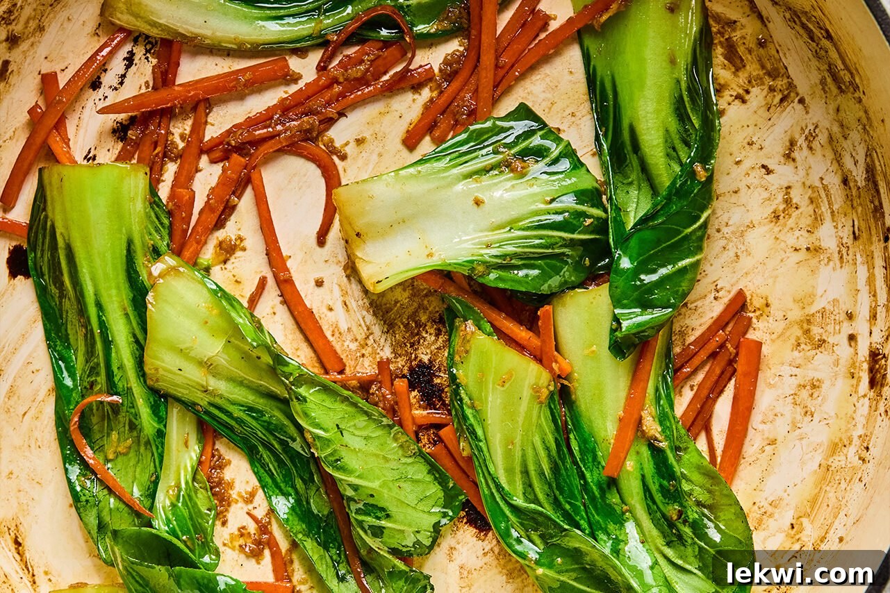 Carrots and baby bok choy sautéing in a pan, releasing their vibrant colors.