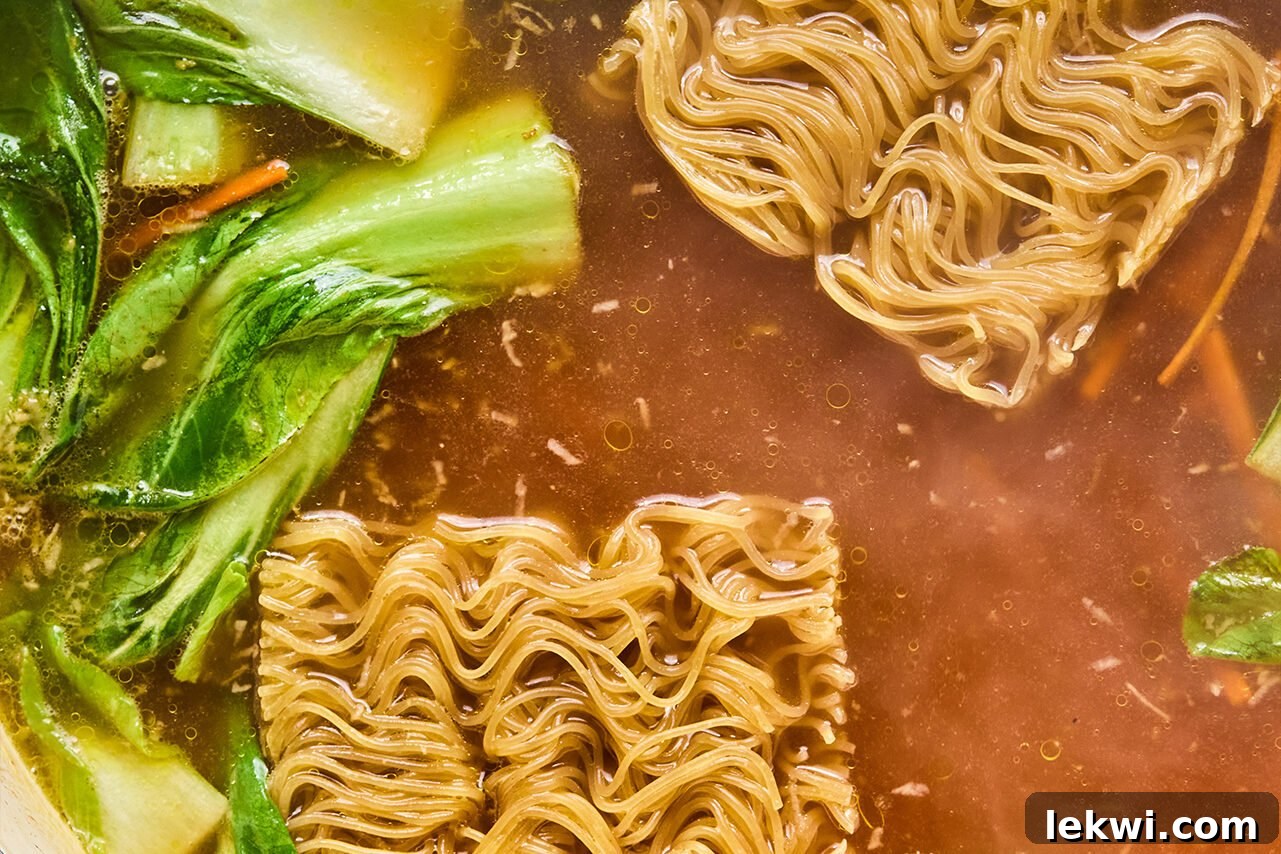 Ramen noodles and rich broth being added to the sautéed bok choy and carrots in the pan.