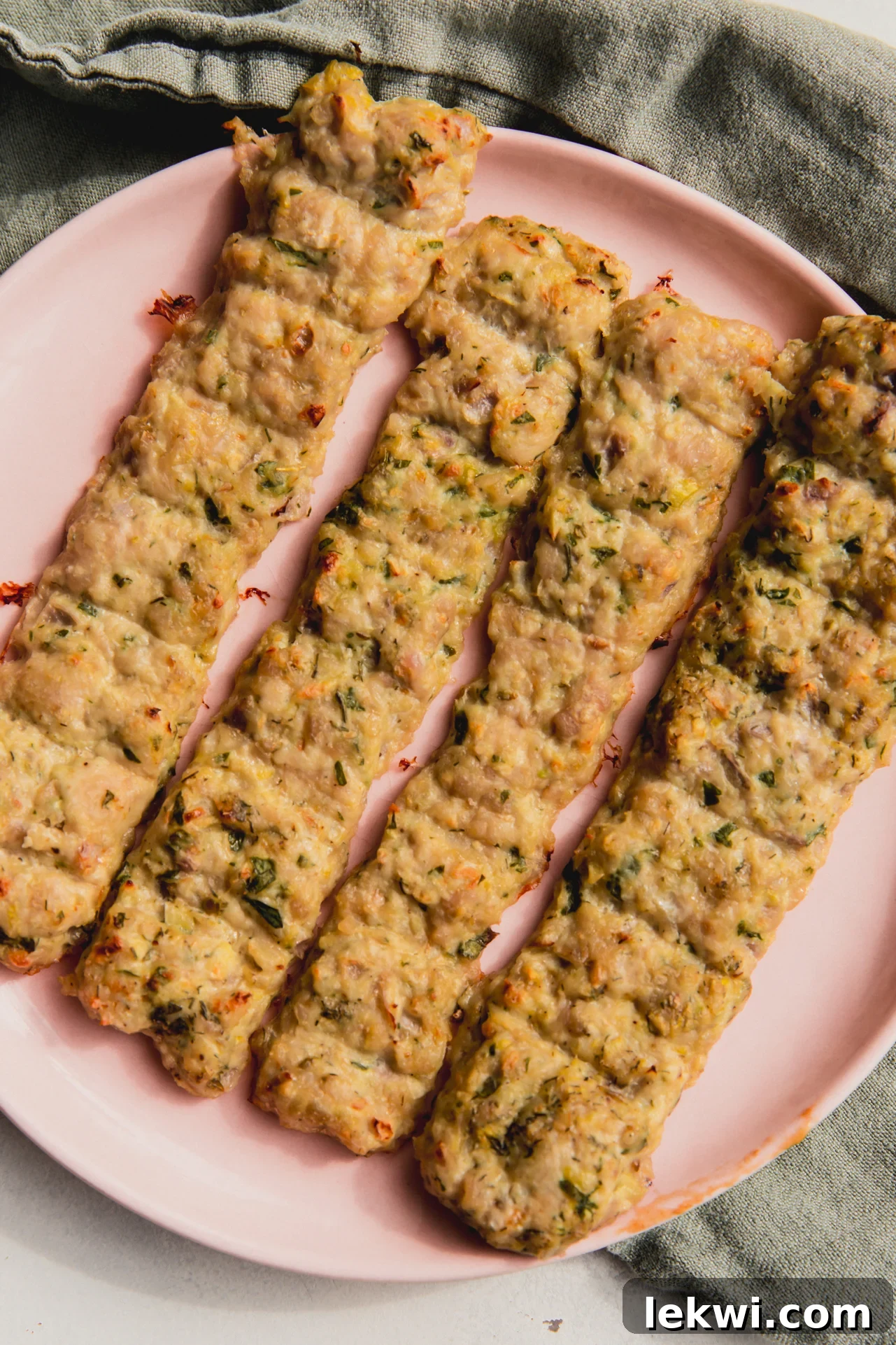 Four sheet pan chicken kebabs on a pink plate, garnished with fresh herbs and lemon wedges.