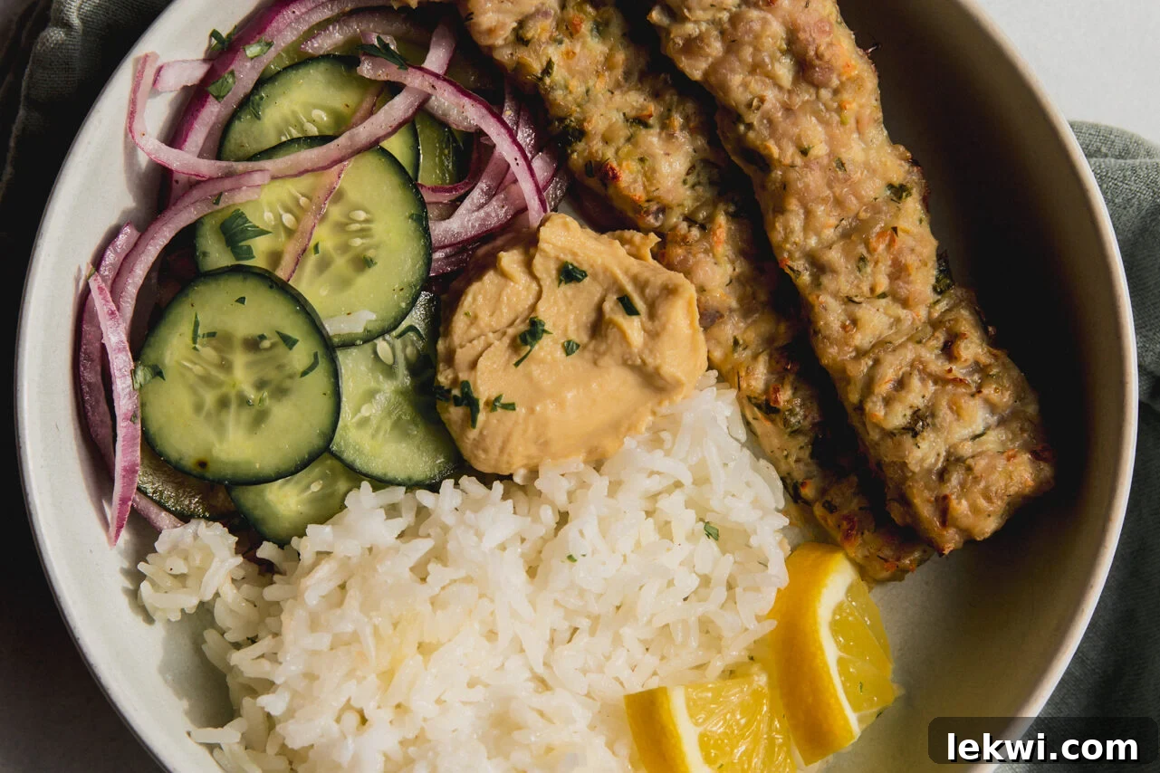 Two sheet pan kebabs in a bowl, served with cucumber salad, white rice, and sliced lemon wedges.