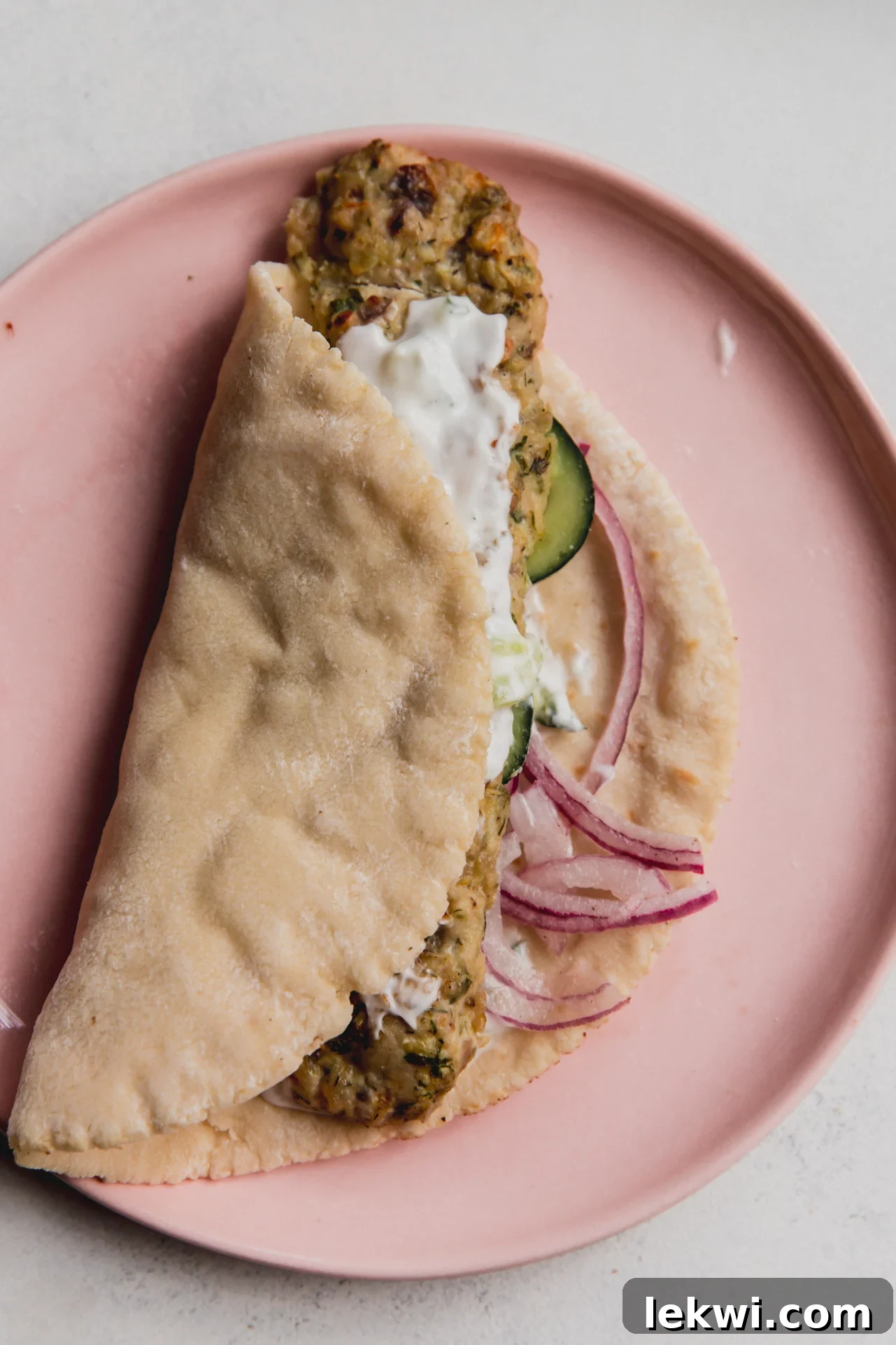 A ground chicken sheet pan kebab wrapped in a pita with cucumber, onion, and a creamy sauce, ready to be eaten.