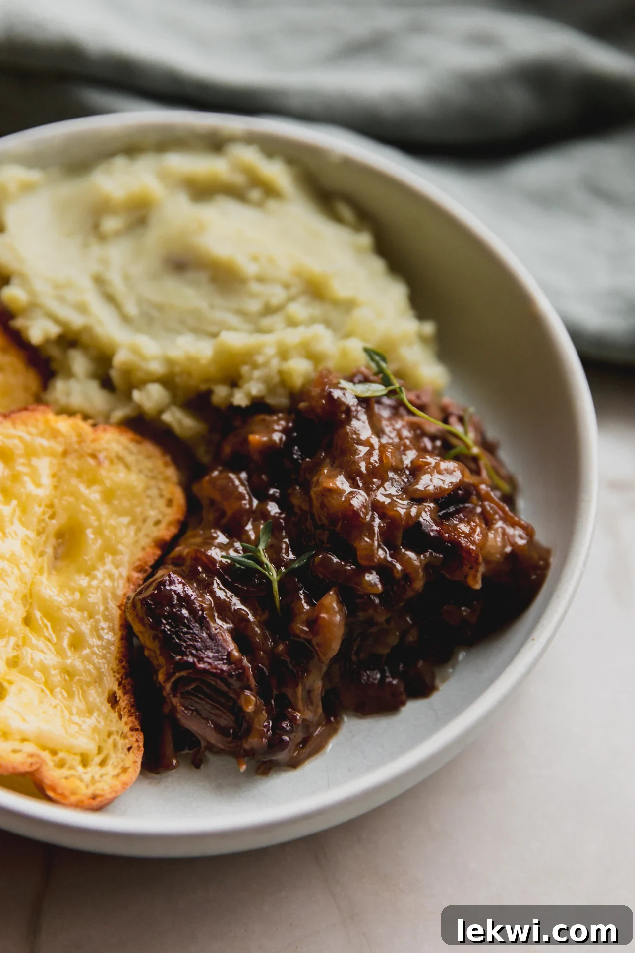 French onion short ribs topped with fresh thyme in a bowl with mashed sweet potato and cheese toast.