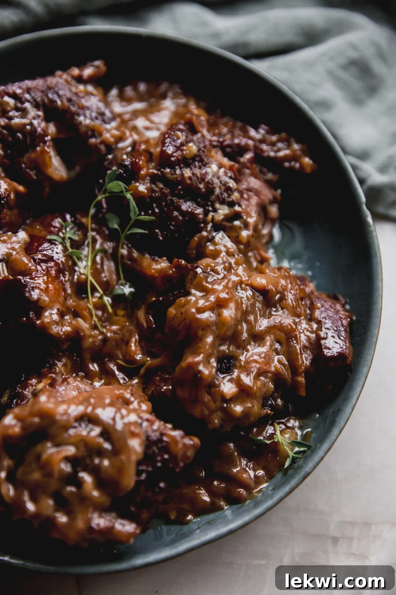 French onion short ribs in a green bowl, shredded and topped with fresh thyme.