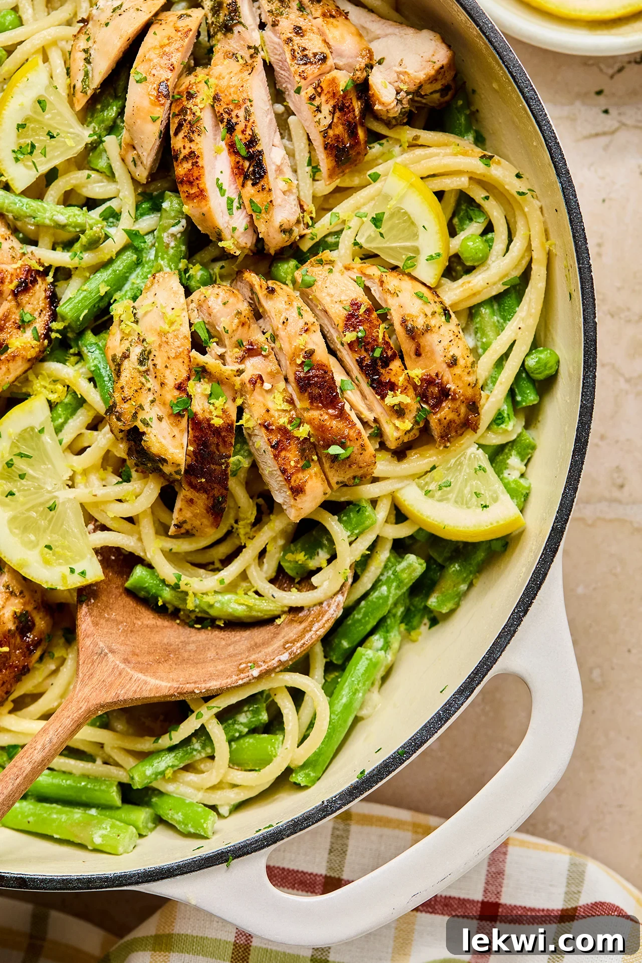 Delicious lemon goat cheese pasta with sliced chicken thighs and vibrant green asparagus and peas in a large white serving pan, garnished with fresh herbs.