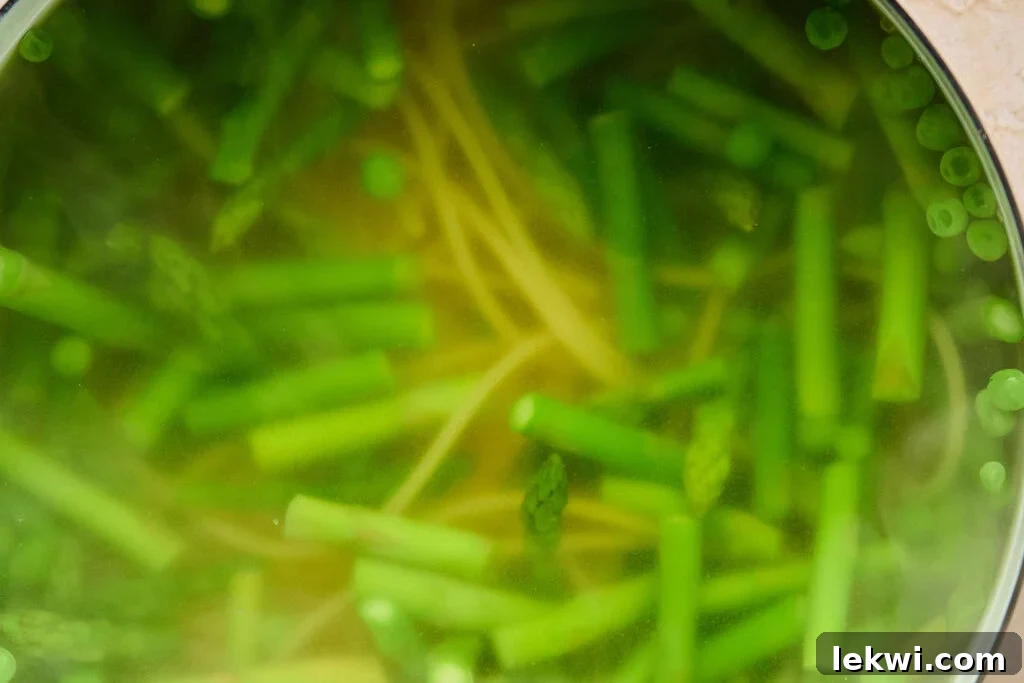 A pot of boiling water with gluten-free pasta, asparagus, and peas cooking together.