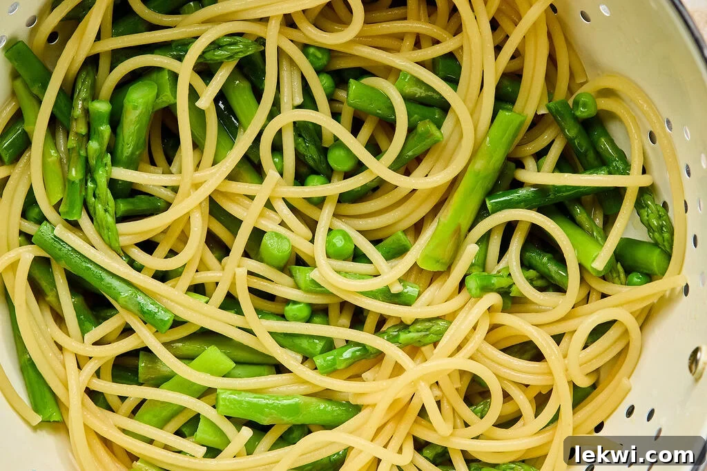 A strainer filled with cooked pasta, peas, and asparagus after being drained.