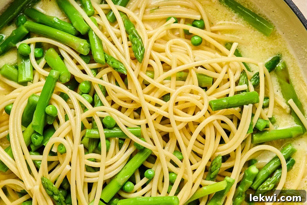 All the cooked ingredients for the lemon goat cheese pasta mixing together in a large pan with the creamy sauce.