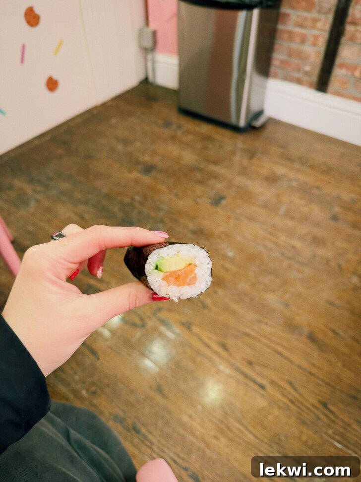 A hand gently holds a freshly prepared salmon and avocado hand roll, showcasing its delicate construction and vibrant ingredients.