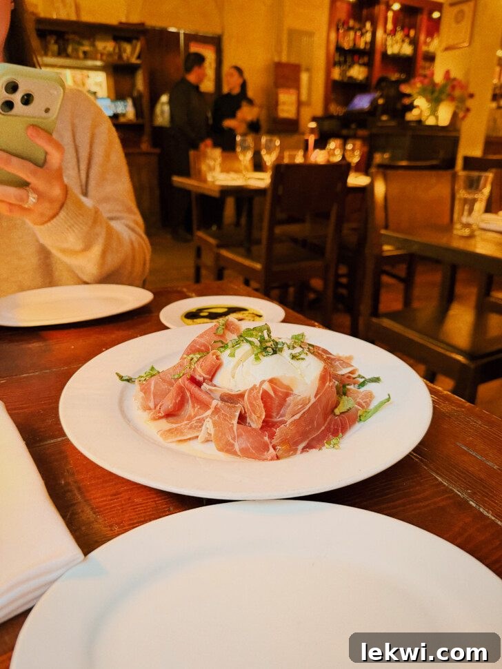 A refined appetizer featuring fresh buffalo mozzarella and thinly sliced prosciutto, elegantly arranged on a plate in a fine dining setting.