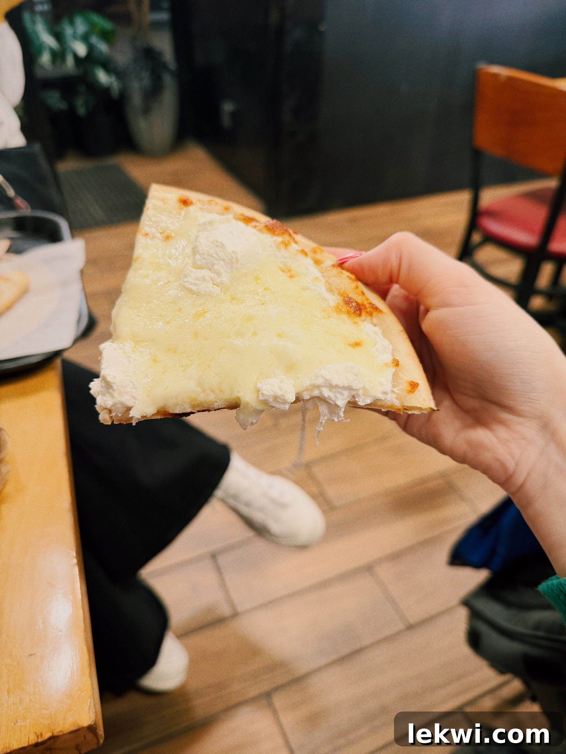 A delicious slice of white pizza with a golden-brown crust and melted cheese, held up against a warm, inviting background.