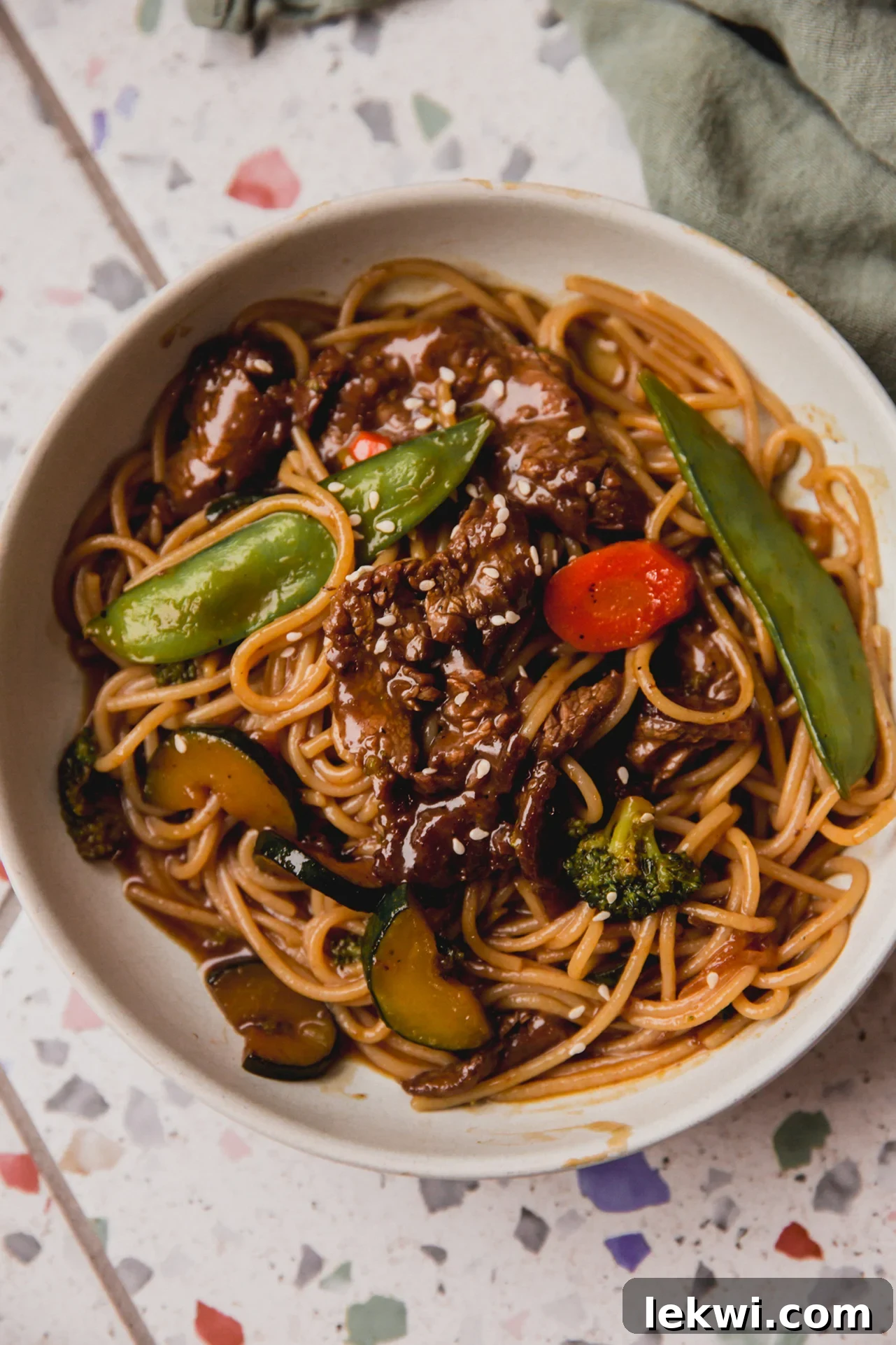 Wok-Tossed Gluten-Free Beef Noodles 2 Steak noodle stir fry in a bowl with veggies and on a colorful surface.