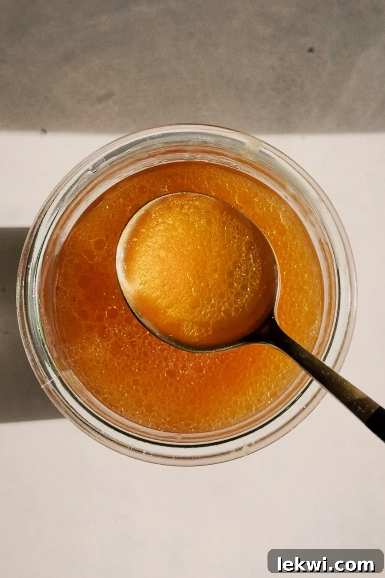 A glass jar filled with rich, golden beef bone broth, with a rustic spoon resting against it, highlighting its nourishing quality.