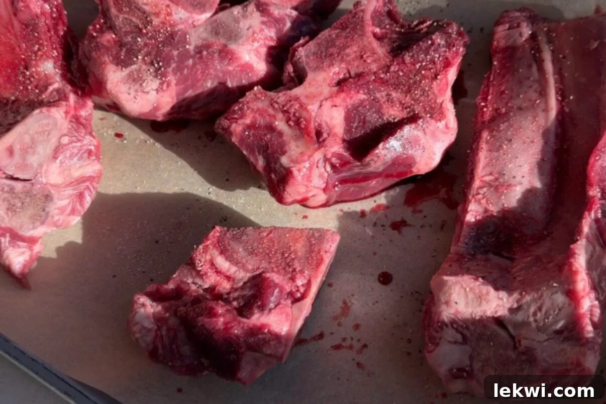 Meaty beef bones precisely arranged on a parchment-lined baking sheet, golden brown and caramelized after roasting, ready to infuse rich flavor.
