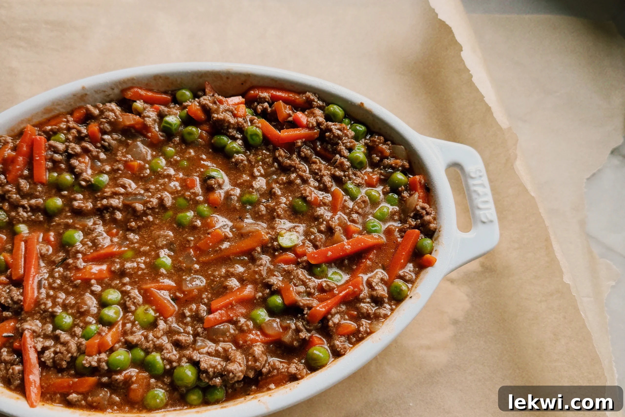 Comforting Gluten-Free Beef Pot Pie 6 Raw cassava flour pie dough being rolled out between two sheets of parchment paper, with a baking dish used as a size guide.