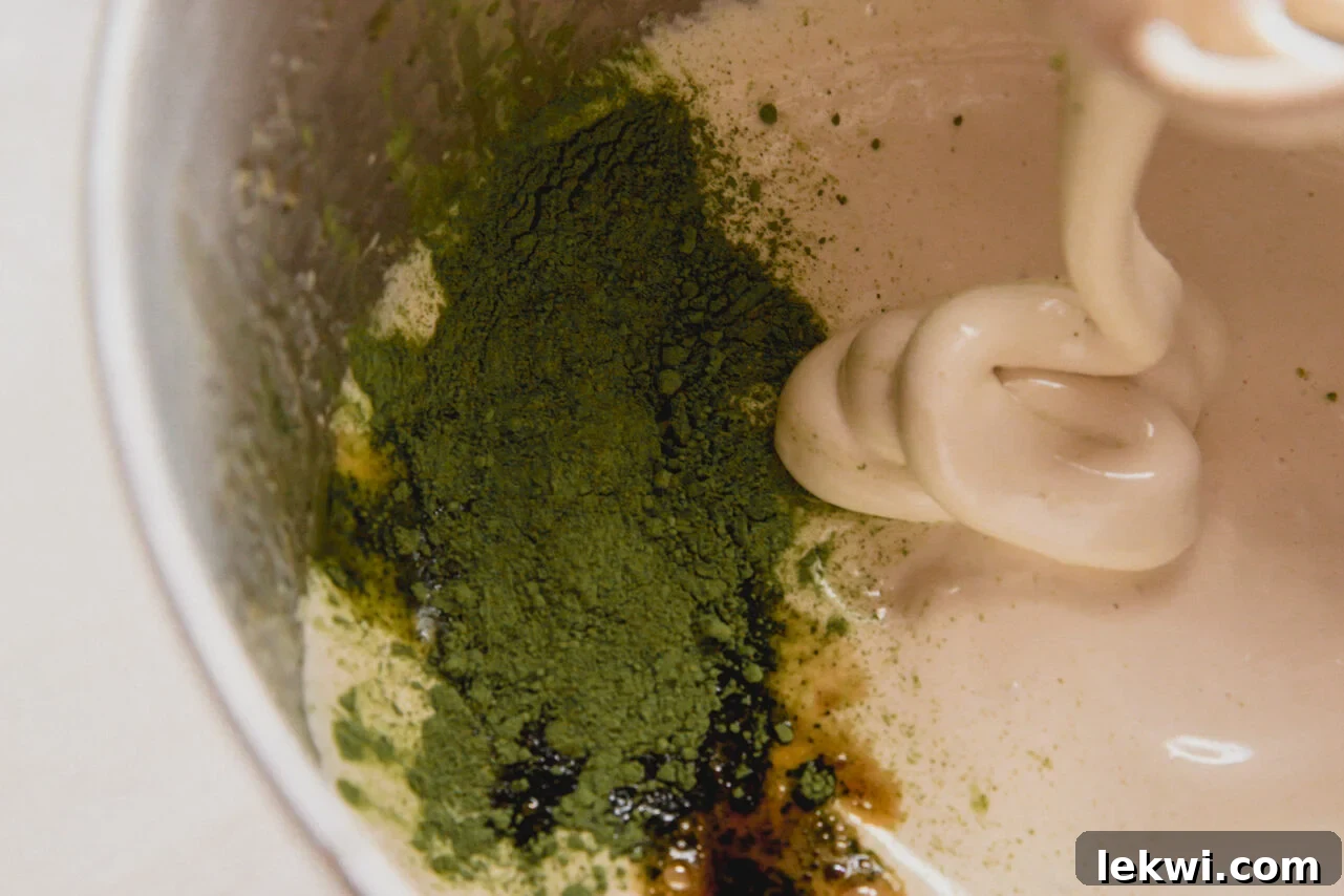 Matcha Mallow Clouds 5 A stand mixer containing the whipped honey, water, and gelatin mixture, now with vanilla extract and sifted matcha powder being added.