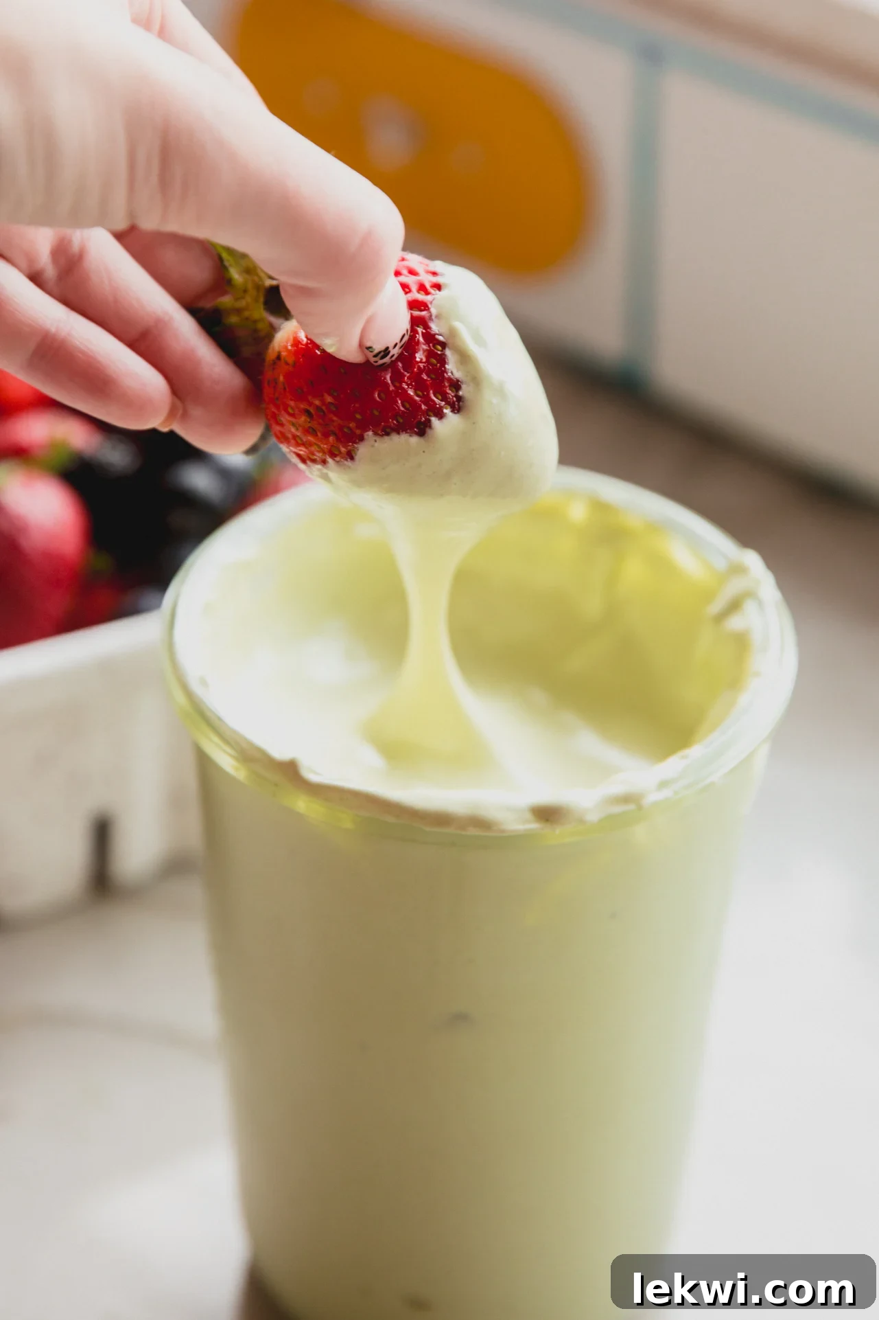 Matcha Mallow Clouds 7 Matcha marshmallow fluff in a jar with a strawberry dipping into it, showcasing its fluffy texture.