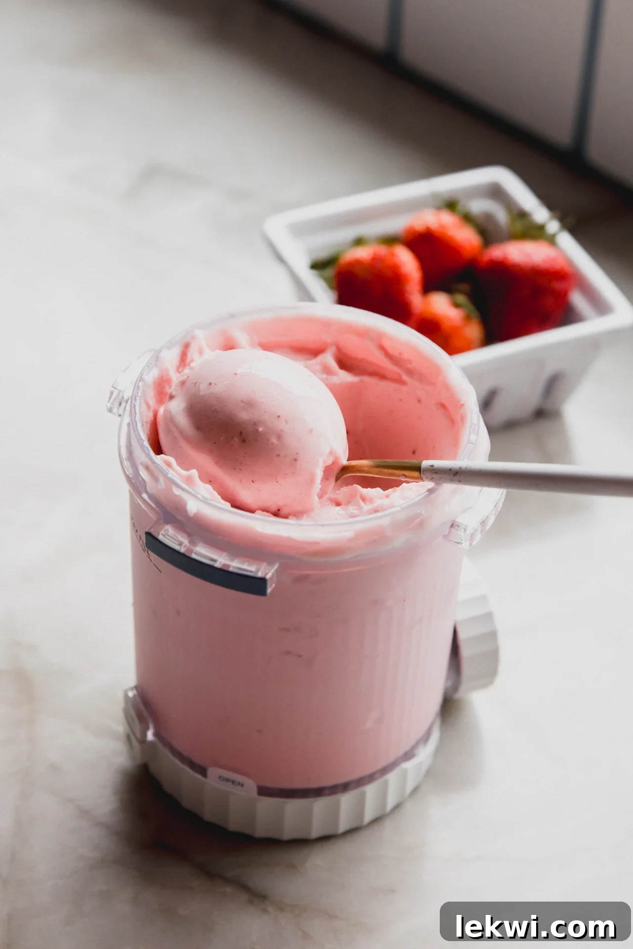 Ninja Creami Dairy Free Strawberry Ice Cream 2 A scoop of creamy Ninja Creami strawberry ice cream being lifted from a clear plastic container, revealing its smooth, soft-serve like consistency and the rich pink hue of fresh strawberries.