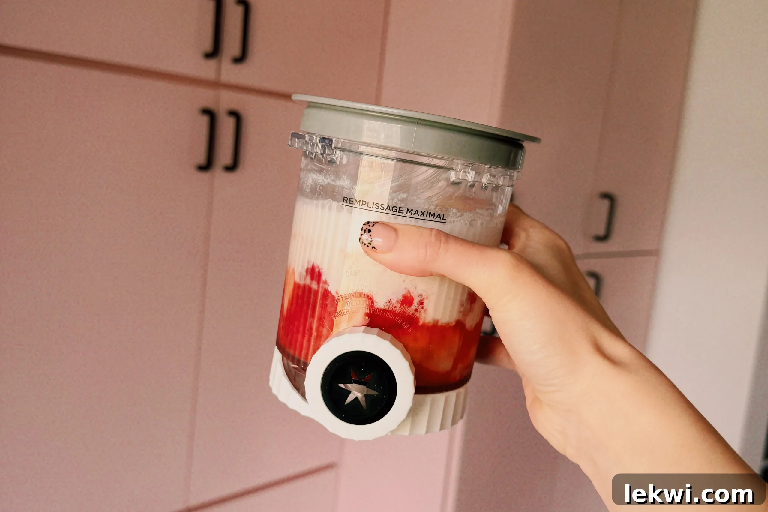 Ninja Creami Dairy Free Strawberry Ice Cream 4 A hand holding a clear Ninja Creami pint container, filled with the vibrant liquid base of strawberry, yogurt, and almond milk, ready to be placed in the freezer.