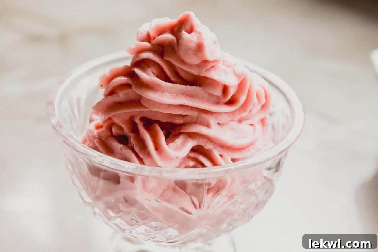 Ninja Creami Dairy Free Strawberry Ice Cream 6 A glistening glass bowl generously filled with perfectly scooped, creamy strawberry ice cream, garnished with a fresh strawberry half, tempting to eat.
