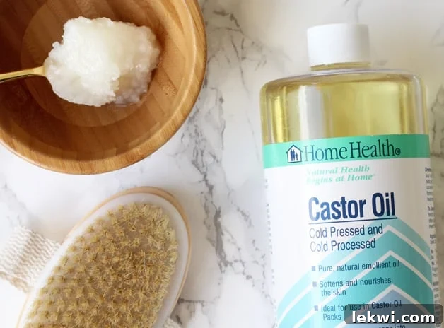 A bottle of castor oil, dry brush, and wooden bowl with oil in it all sitting together on a counter.