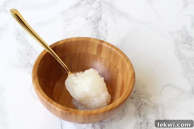 A small wooden bowl with a spoon filled with coconut oil in it.