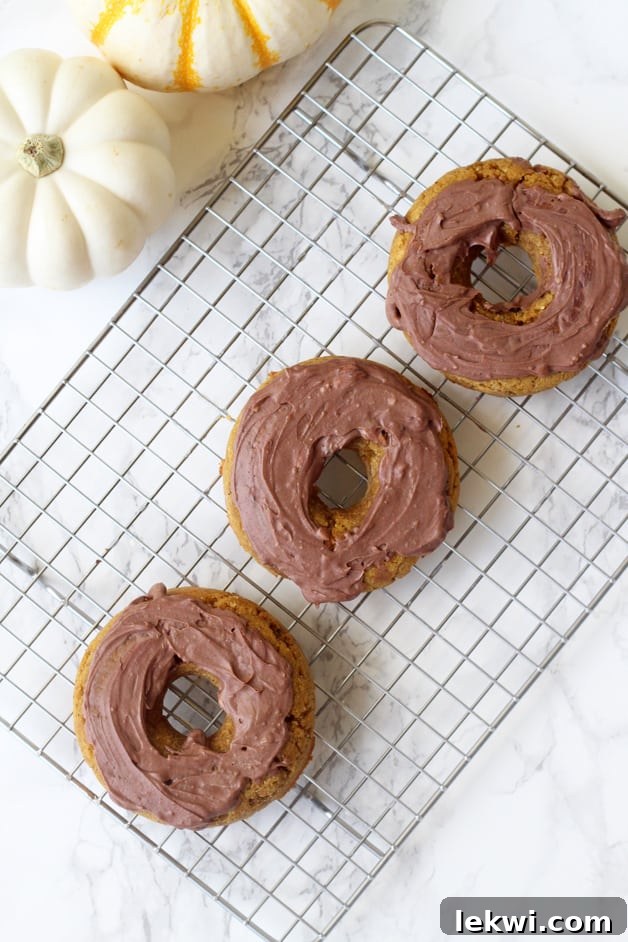 Three paleo pumpkin donuts, freshly frosted and cooling on a wire rack, ready to be enjoyed.