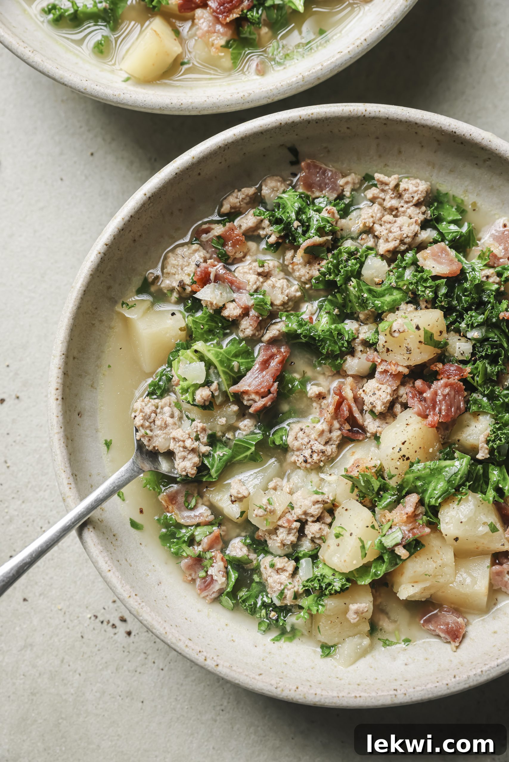 Spoon scooping creamy Instant Pot Zuppa Toscana from a bowl, highlighting sausage, kale, and potatoes.