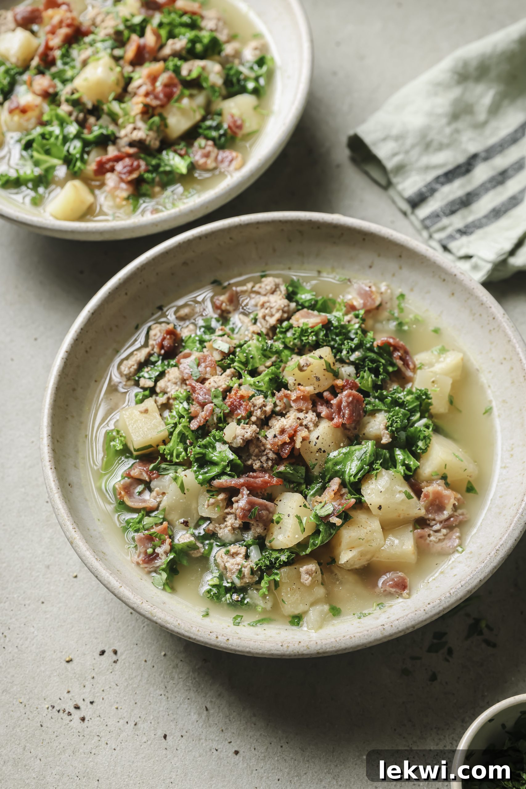Two bowls of Zuppa Toscana garnished with bacon and parsley, ready to be served.