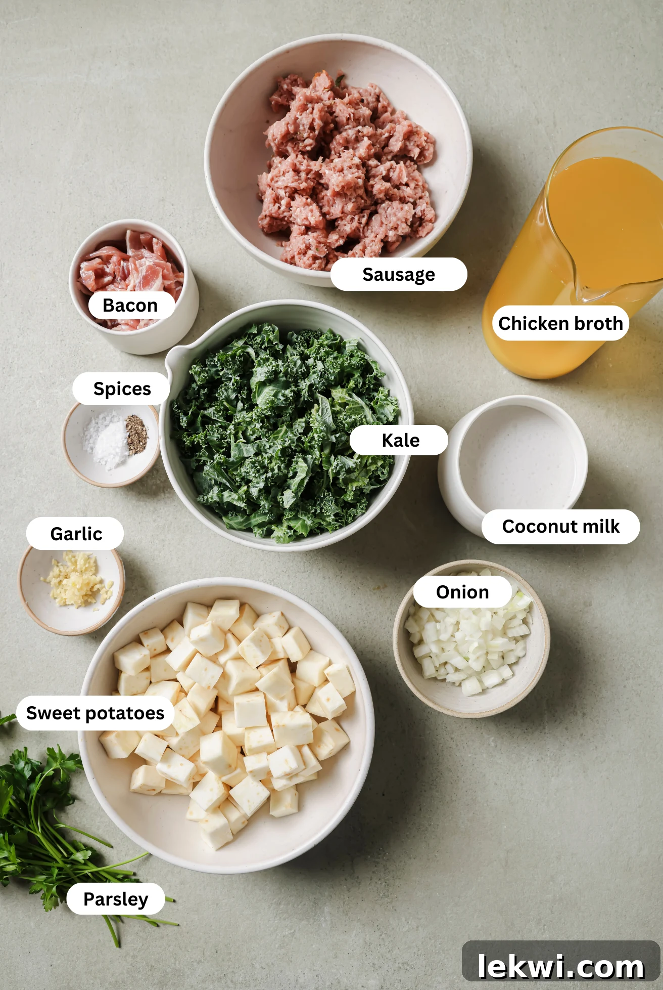 All the ingredients for Zuppa Toscana laid out before cooking, including sausage, bacon, onion, garlic, sweet potatoes, kale, broth, and coconut milk.