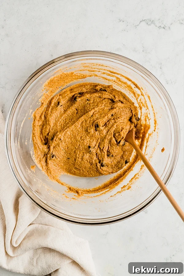 A bowl of pumpkin chocolate chip cookie skillet dough, showing its texture and chocolate chips, with a wooden spoon resting in it.
