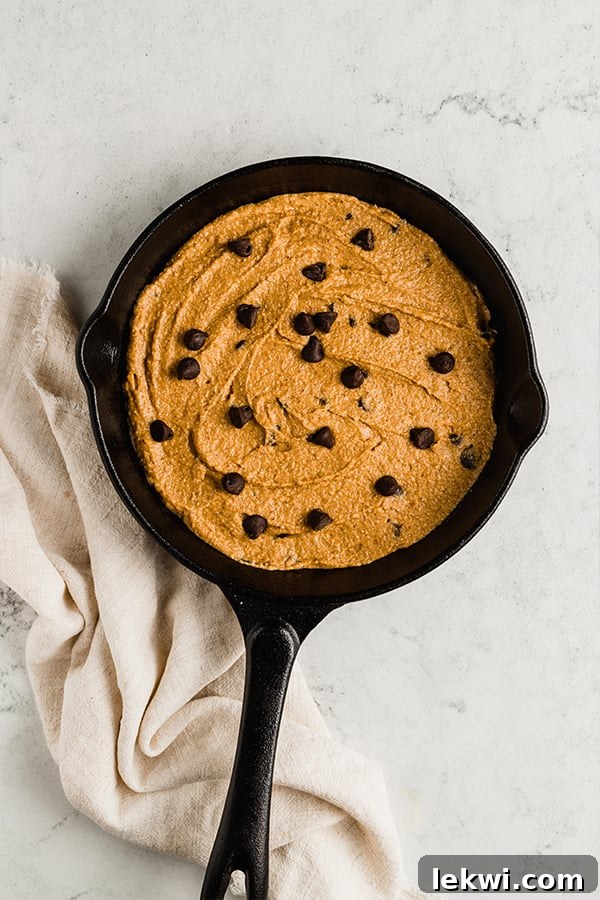 A mini cast iron skillet filled with unbaked pumpkin chocolate chip cookie skillet dough, ready for the oven.