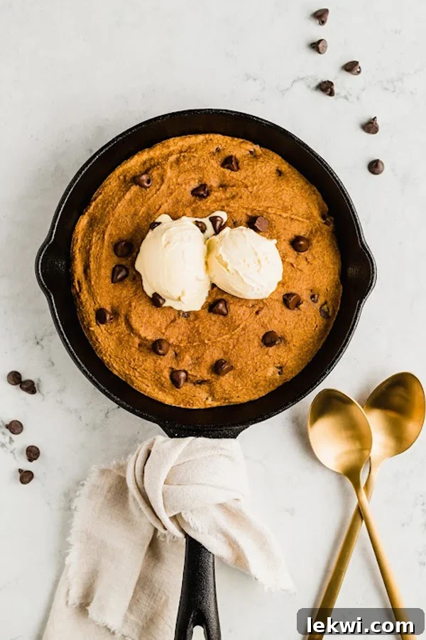 The baked pumpkin chocolate chip cookie skillet, still in the pan, generously topped with a scoop of melting coconut milk ice cream.