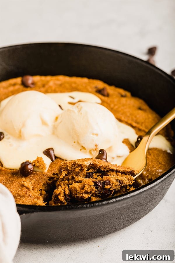 A close-up view of the warm pumpkin chocolate chip cookie skillet, topped with a scoop of coconut milk ice cream, showcasing its irresistible texture.