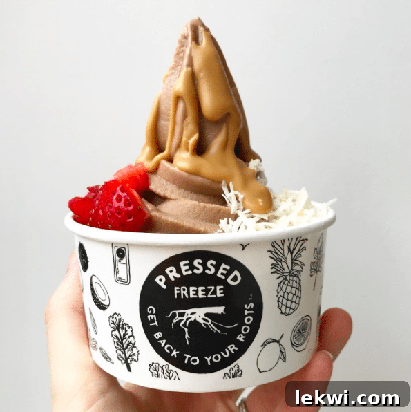 A cup from Pressed Juicery featuring a dairy-free freeze topped with a generous peanut butter drizzle, fresh strawberries, and shredded coconut.