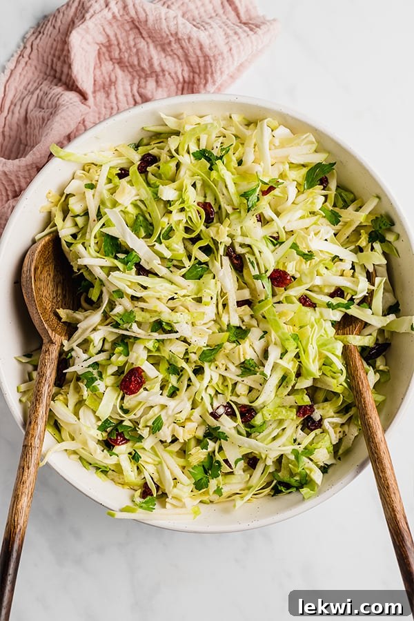 A beautifully arranged Thanksgiving coleslaw in a white serving bowl, garnished with fresh parsley and surrounded by wooden serving spoons.