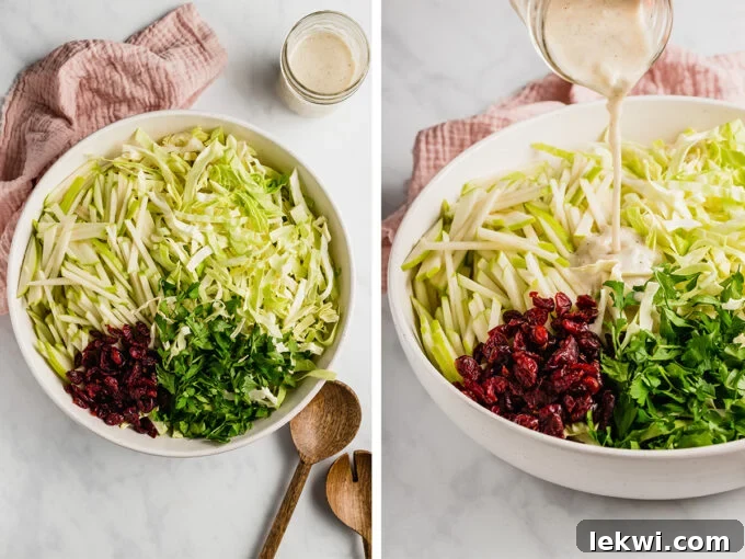Close-up shot of creamy Thanksgiving coleslaw dressing being poured into a bowl of shredded cabbage, apples, cranberries, and parsley, with wooden serving spoons nearby.