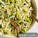 A white serving bowl filled with Thanksgiving coleslaw with wooden serving spoons.