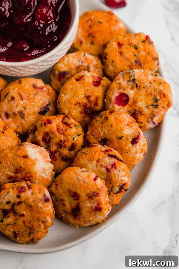 A close-up shot of cranberry sweet potato turkey poppers on a white plate, with a bowl of cranberry sauce, showcasing their appealing golden exterior and festive appeal.