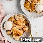 Two bowls filled with apple crisp and coconut ice cream and a spoon.