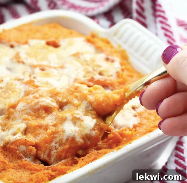A baking dish filled with sweet potato casserole with a spoon taking a spoonful out.