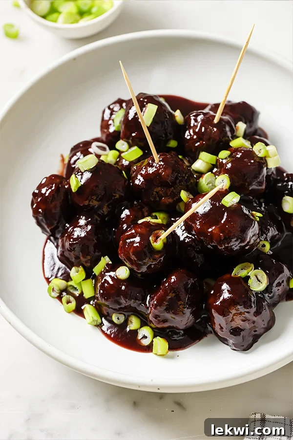 Pile of cocktail meatballs with grape jelly on a plate.